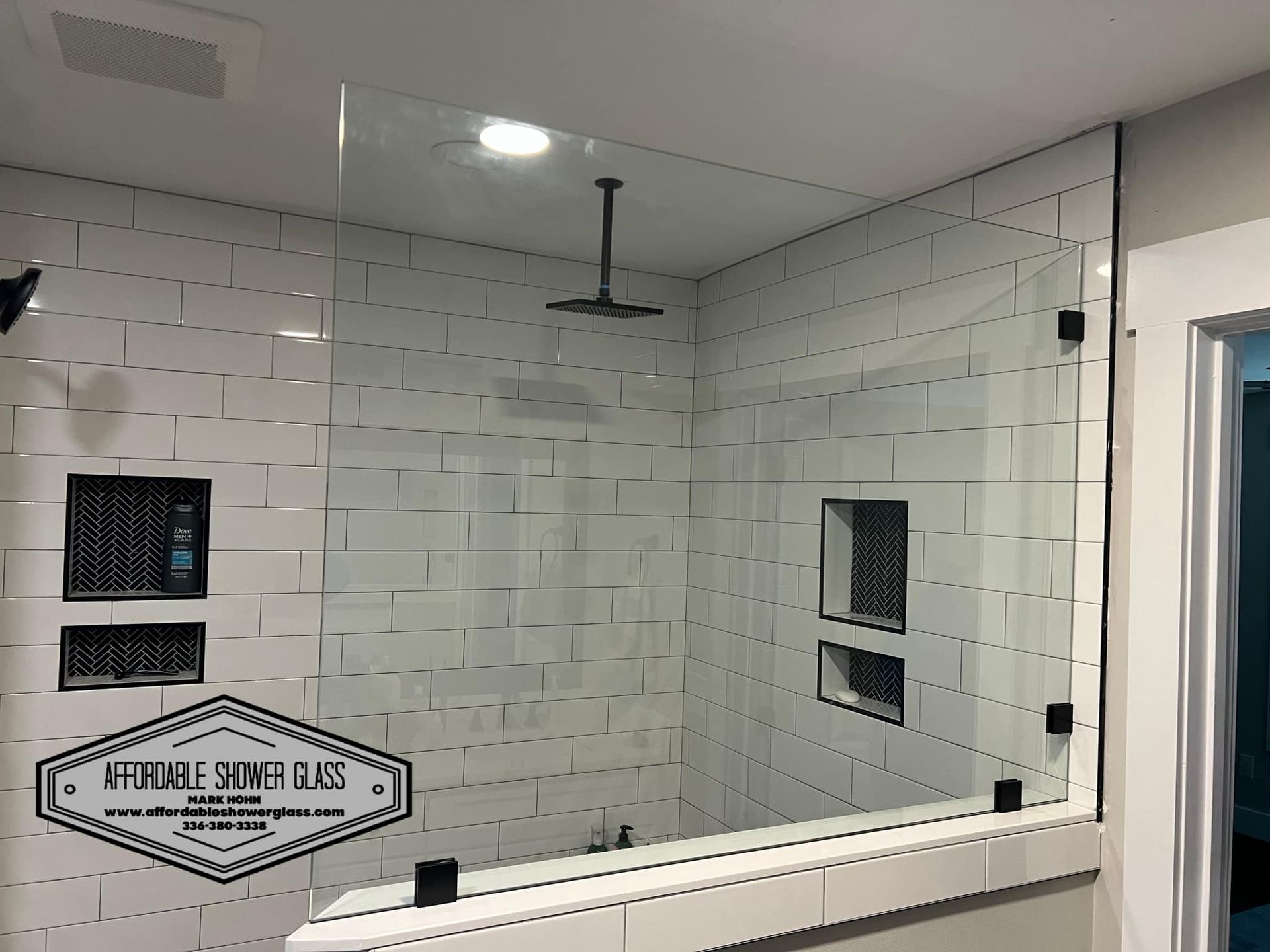 A bathroom with white tiles and a glass shower door.