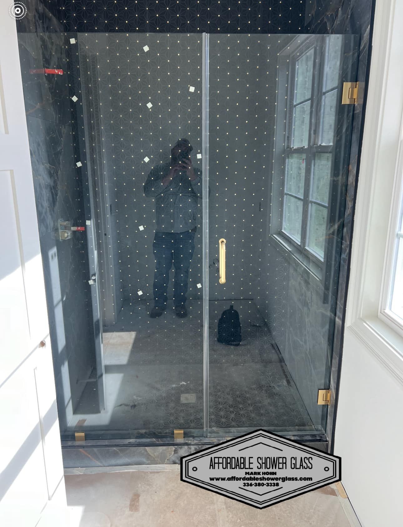 A man is taking a picture of himself in a glass shower door.