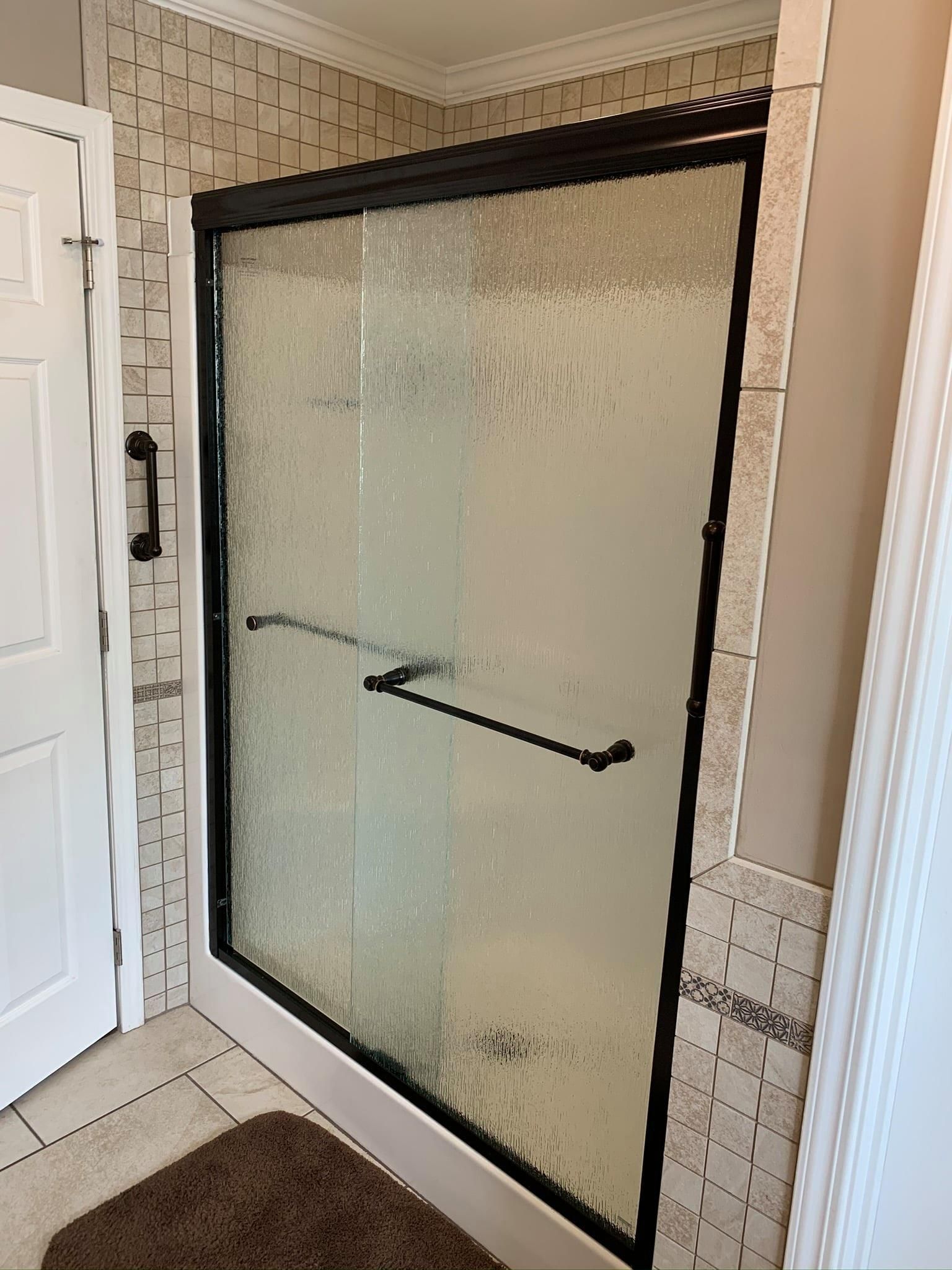 A bathroom with a sliding glass shower door and a brown rug.