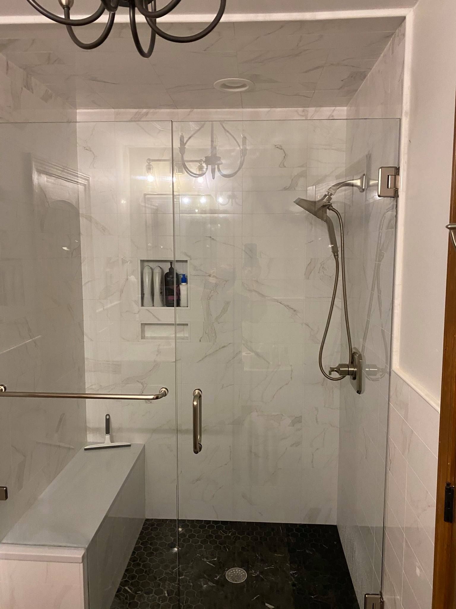 A bathroom with a walk in shower with a glass door and a bench.