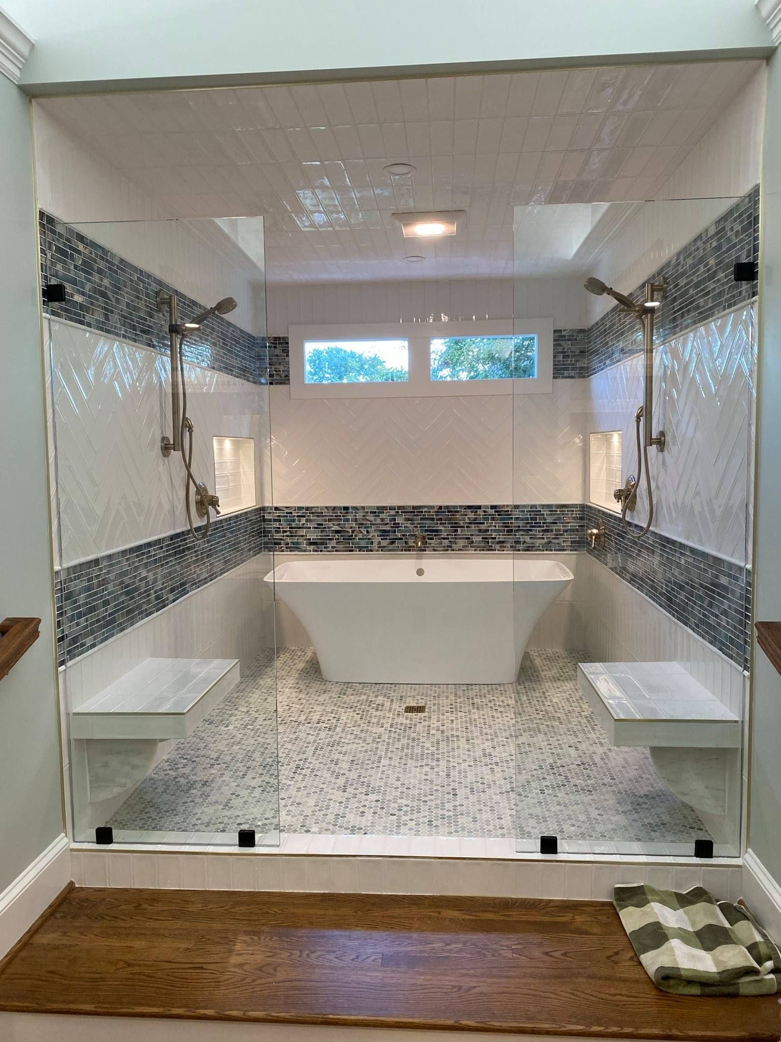 A bathroom with a tub, shower, benches and a glass door.