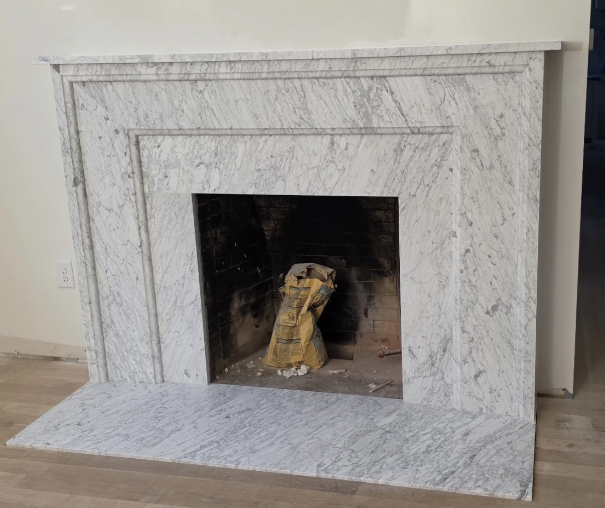 White marble fireplace surround with a black firebox and stone hearth in a bare room