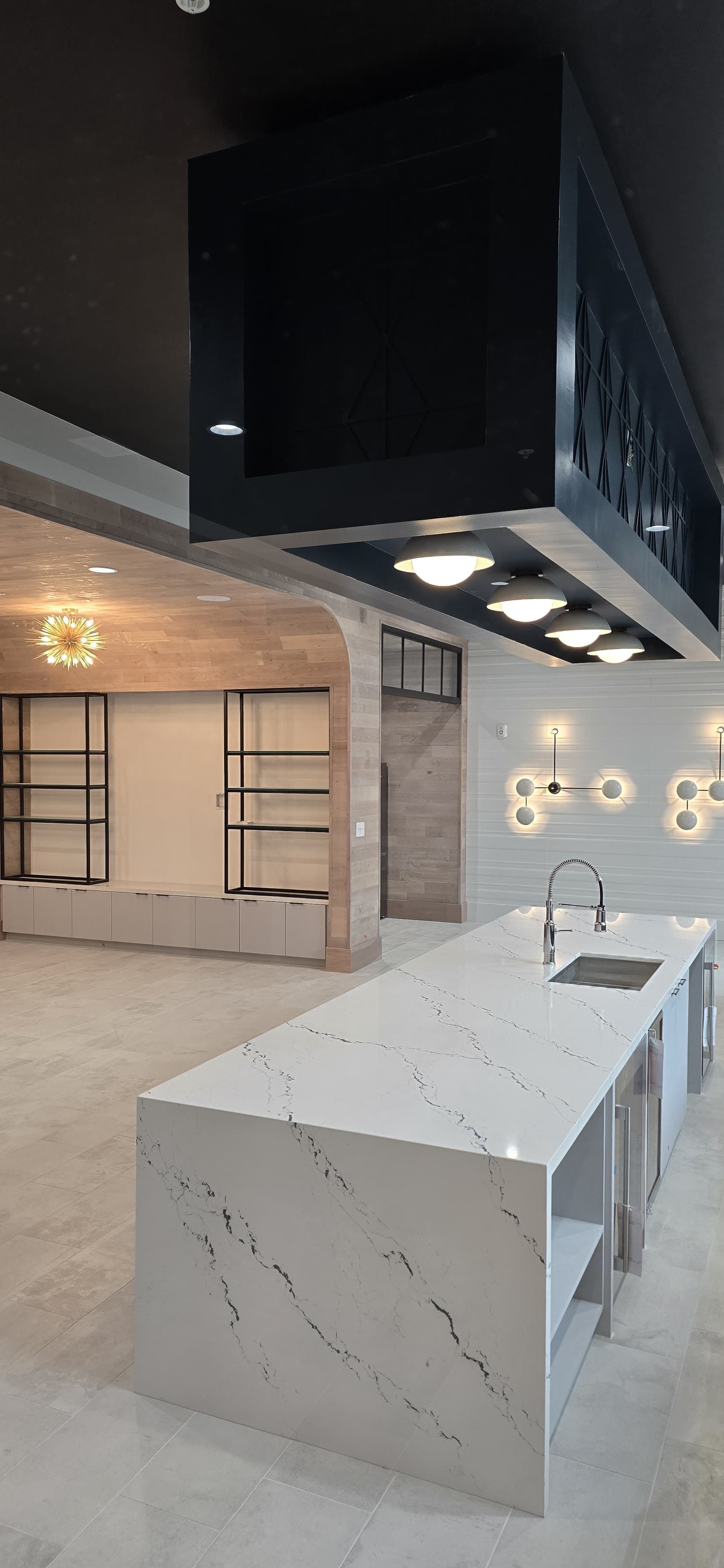Modern kitchen with marble island, black range hood, and pendant lights in an open living space