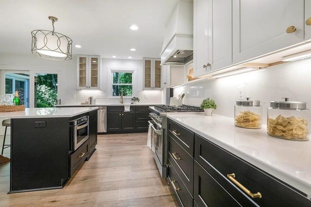 A modern kitchen featuring a dark island and base cabinets, white upper cabinets, light countertops, and wood flooring.