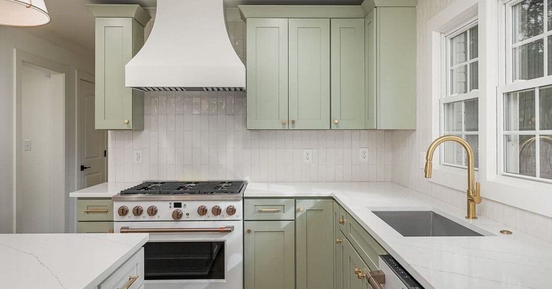 Green kitchen with white countertops and backsplash, gold faucet.