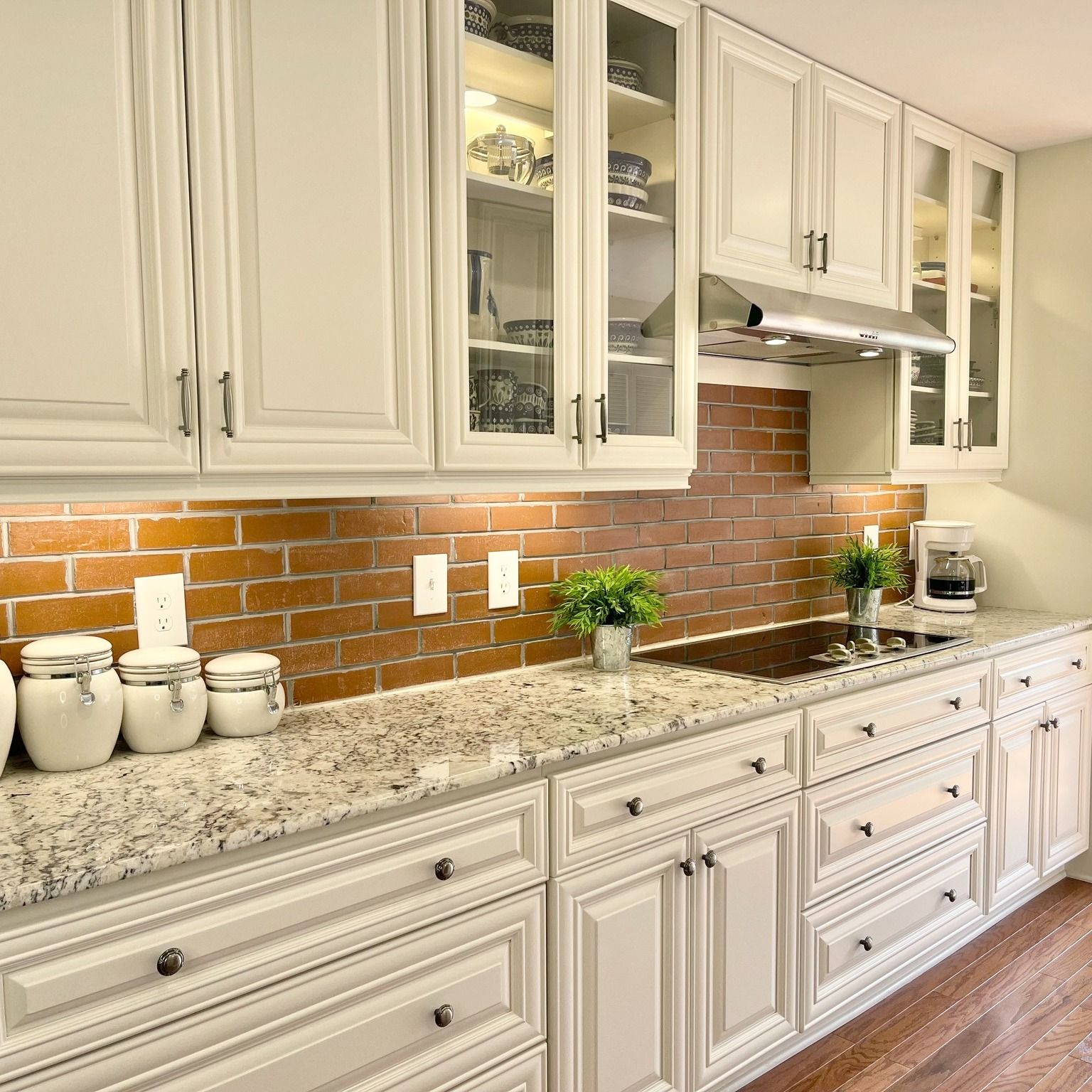 White kitchen cabinets with glass doors, brick backsplash, and granite countertop.