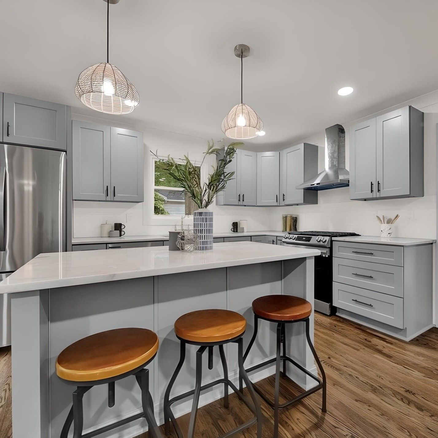 Gray kitchen with island and bar stools, stainless steel appliances, and pendant lights.