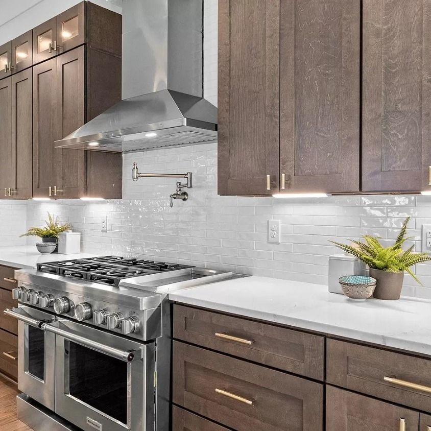 Modern kitchen with stainless steel appliances, dark wood cabinets, white countertops and backsplash.