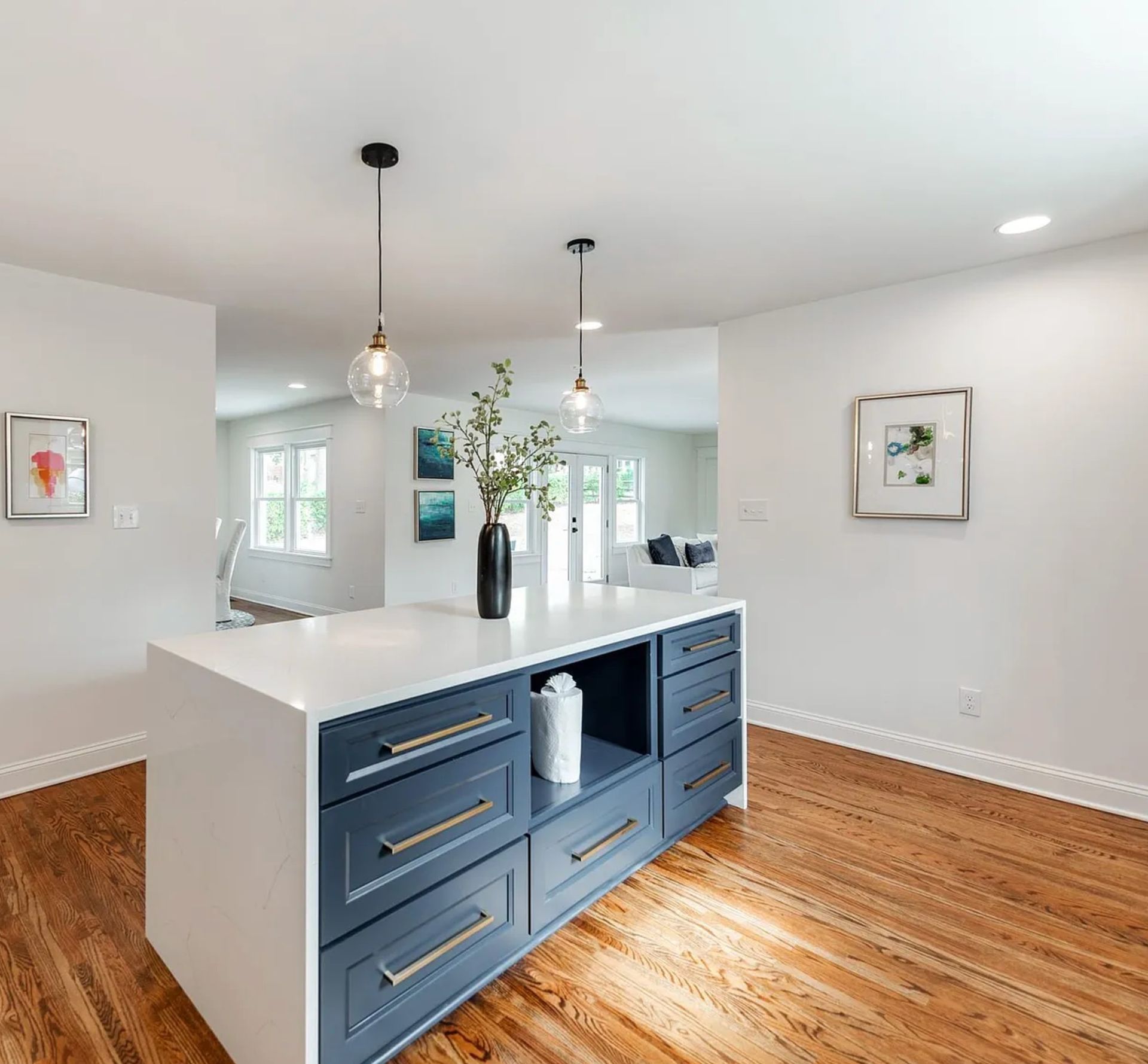Kitchen with navy blue island, white countertop, pendant lights, hardwood floors.