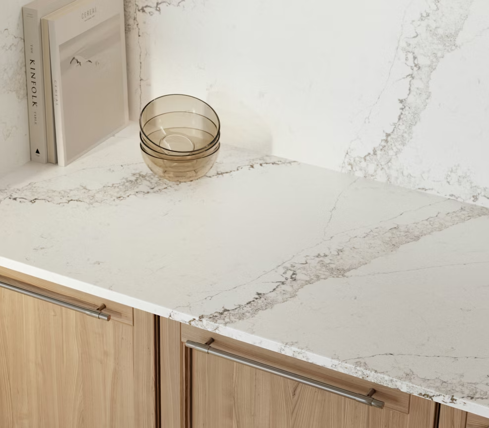 Light wood cabinets with a white countertop and decorative glass bowls and books.