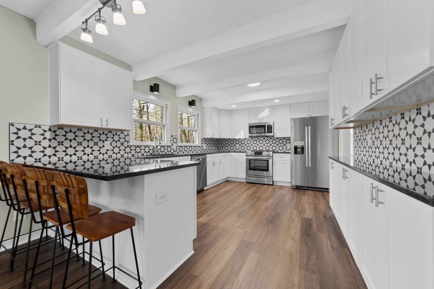 Modern white kitchen with wood floors, black countertops, and mosaic tile backsplash.