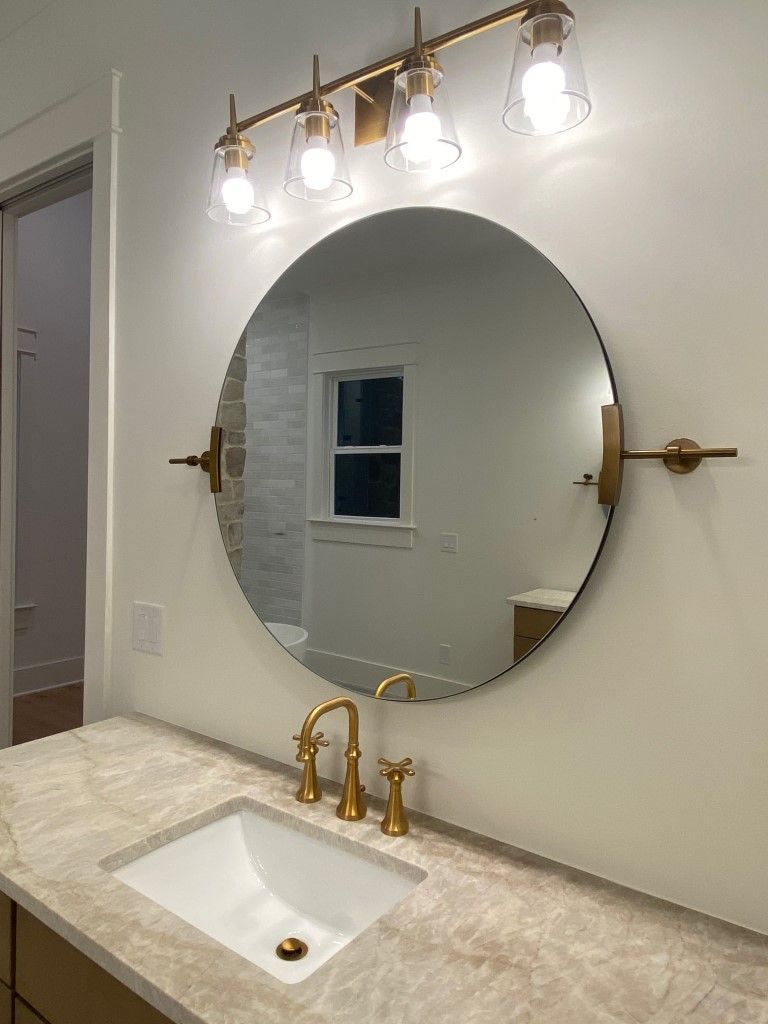 Bathroom vanity with a round mirror, gold fixtures, and a four-light fixture.