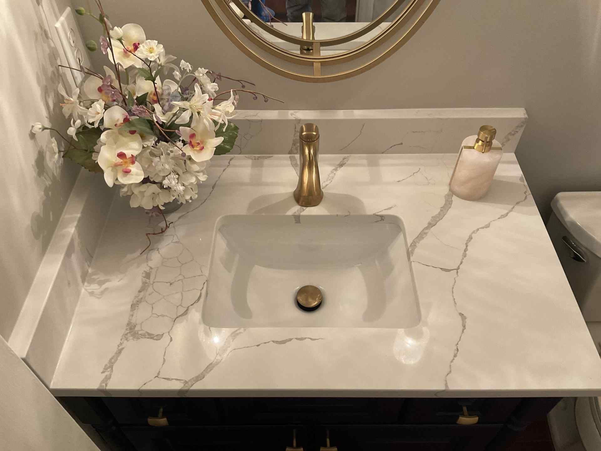 White marble countertop with gold fixtures, a white sink, and floral arrangement.