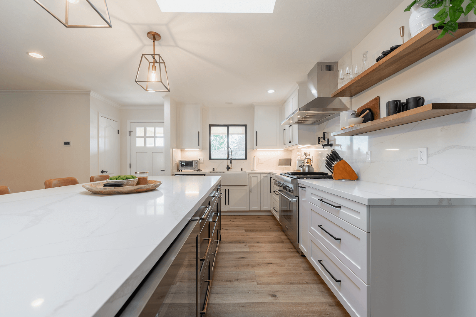 Modern white kitchen with island, stainless steel appliances, and wooden shelves.