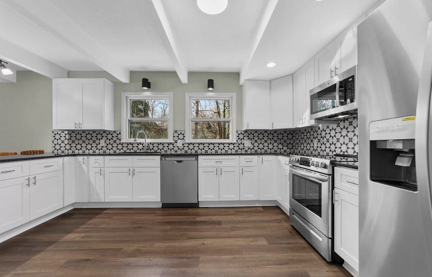 Modern white kitchen with stainless steel appliances and dark wood flooring.