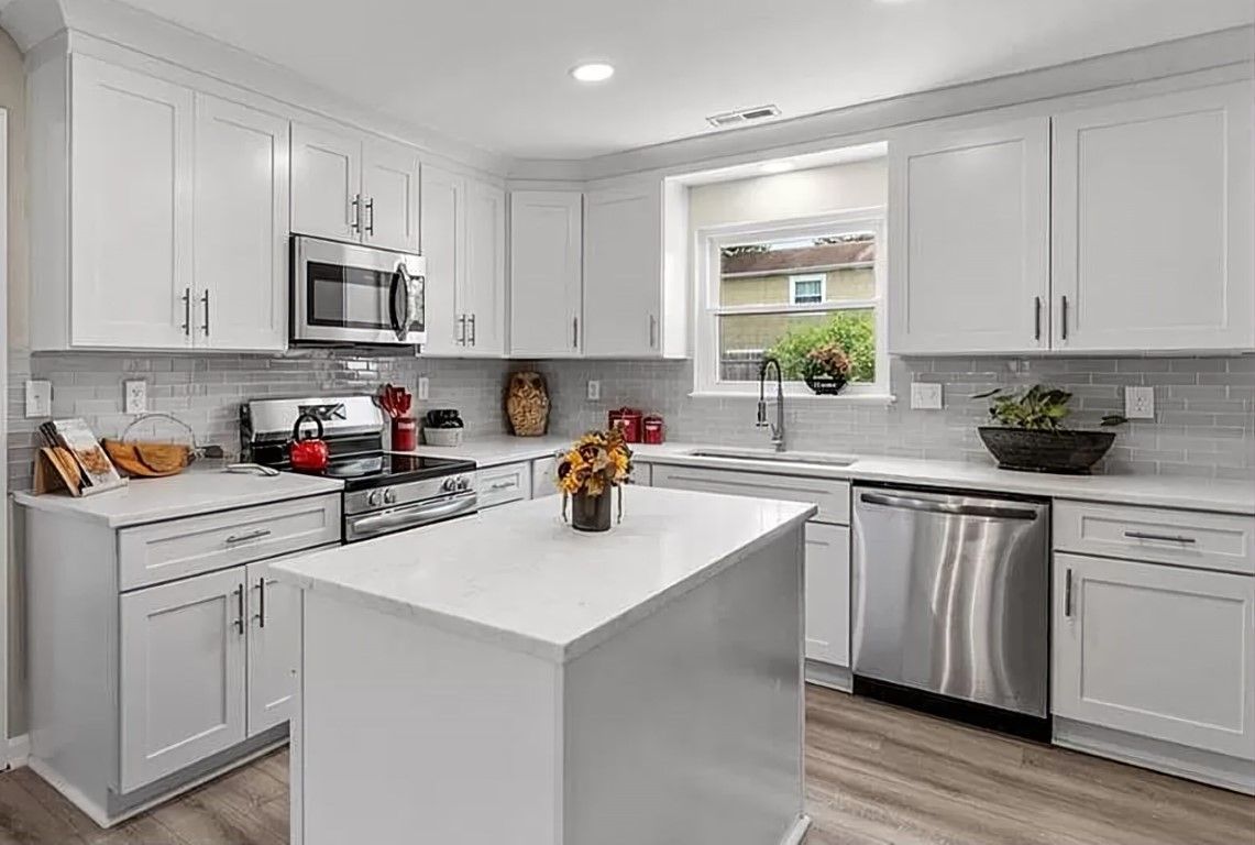 Bright white kitchen with stainless steel appliances, white cabinets, and a kitchen island.