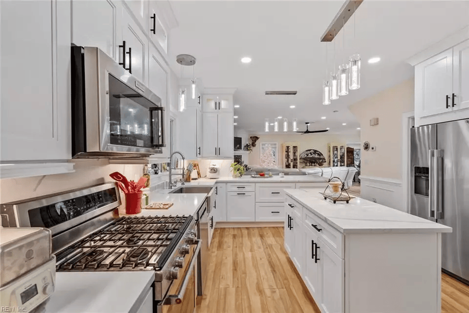 White kitchen with stainless steel appliances, white cabinets, and island with black hardware and wood floor.