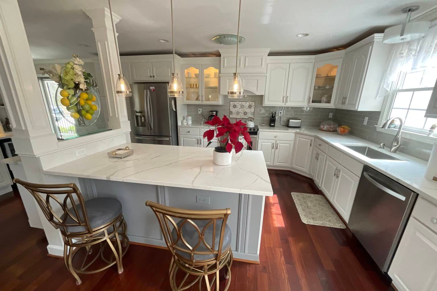 Bright white kitchen with a peninsula and bar seating, stainless steel appliances, and wood floors.