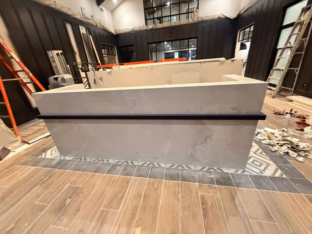 Construction site with a large concrete counter. Wood flooring, tile border, ladders, and tools visible.
