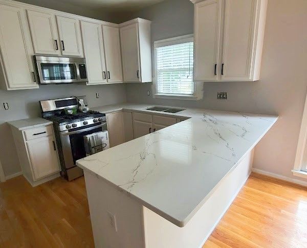 White kitchen with quartz countertops, stainless steel appliances, and wood flooring.