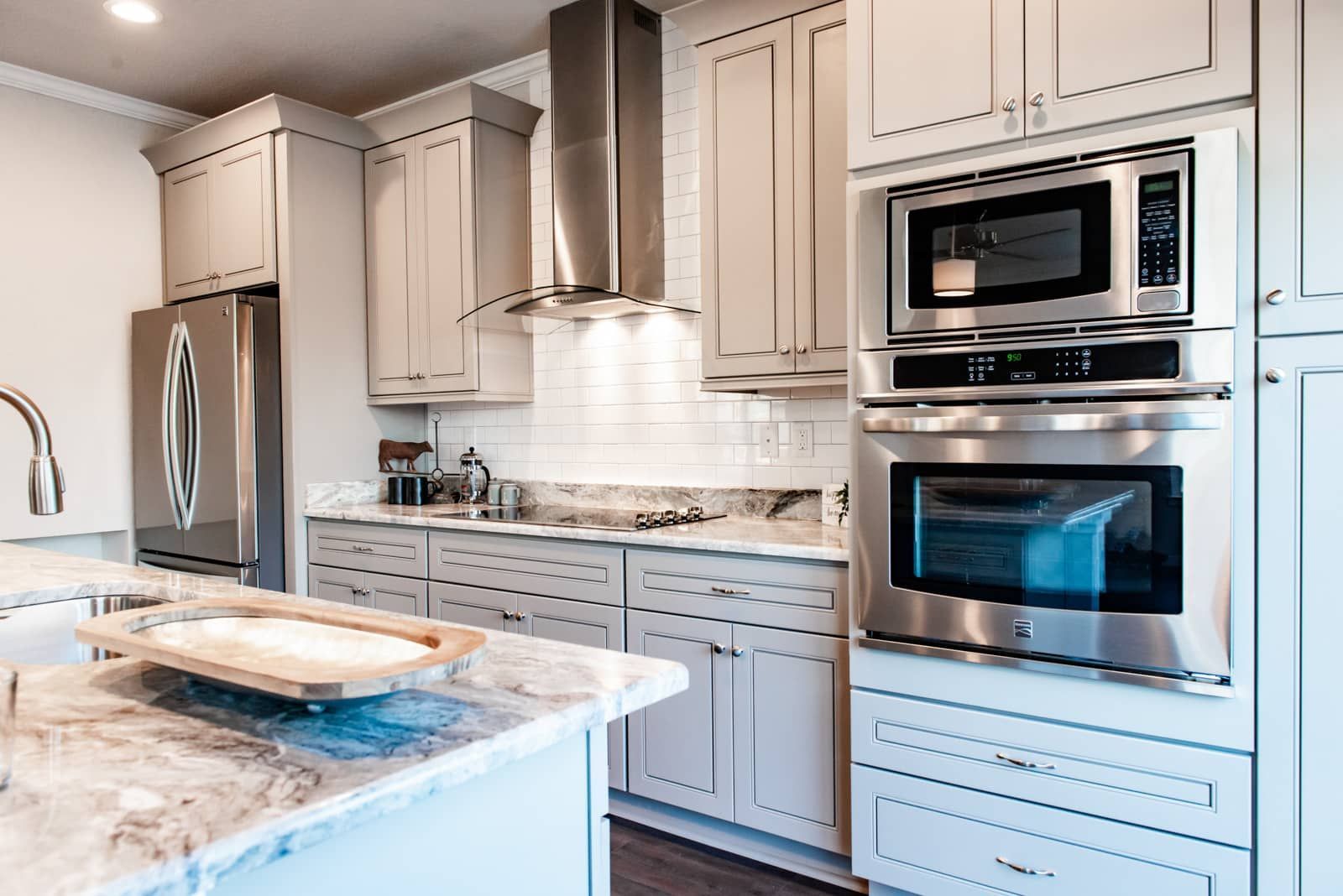 Modern kitchen with light gray cabinets, stainless steel appliances, and a marble countertop island.
