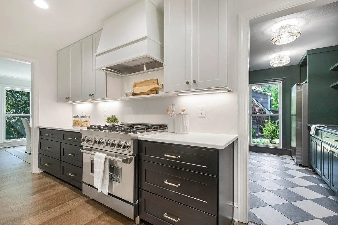 Modern kitchen with dark lower cabinets and light uppers, stainless steel appliances, and a view into another room.