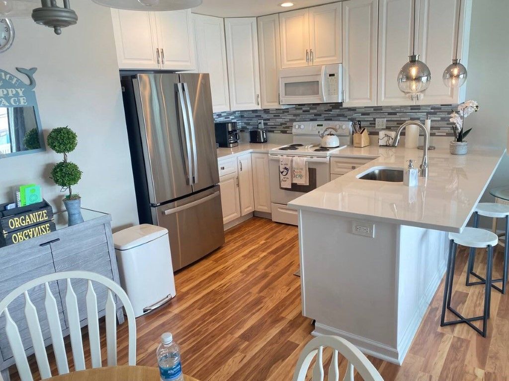 A bright, white kitchen with stainless steel appliances, a breakfast bar, and hardwood floors.