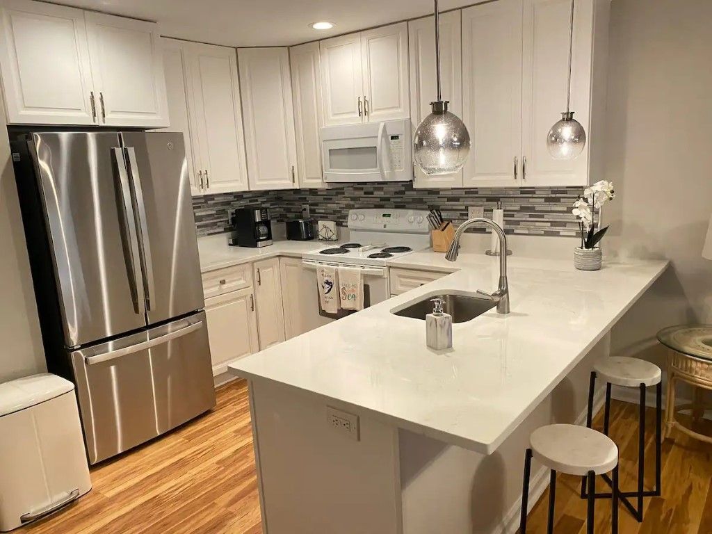 White kitchen with stainless steel appliances, breakfast bar, pendant lights, and wood floors.