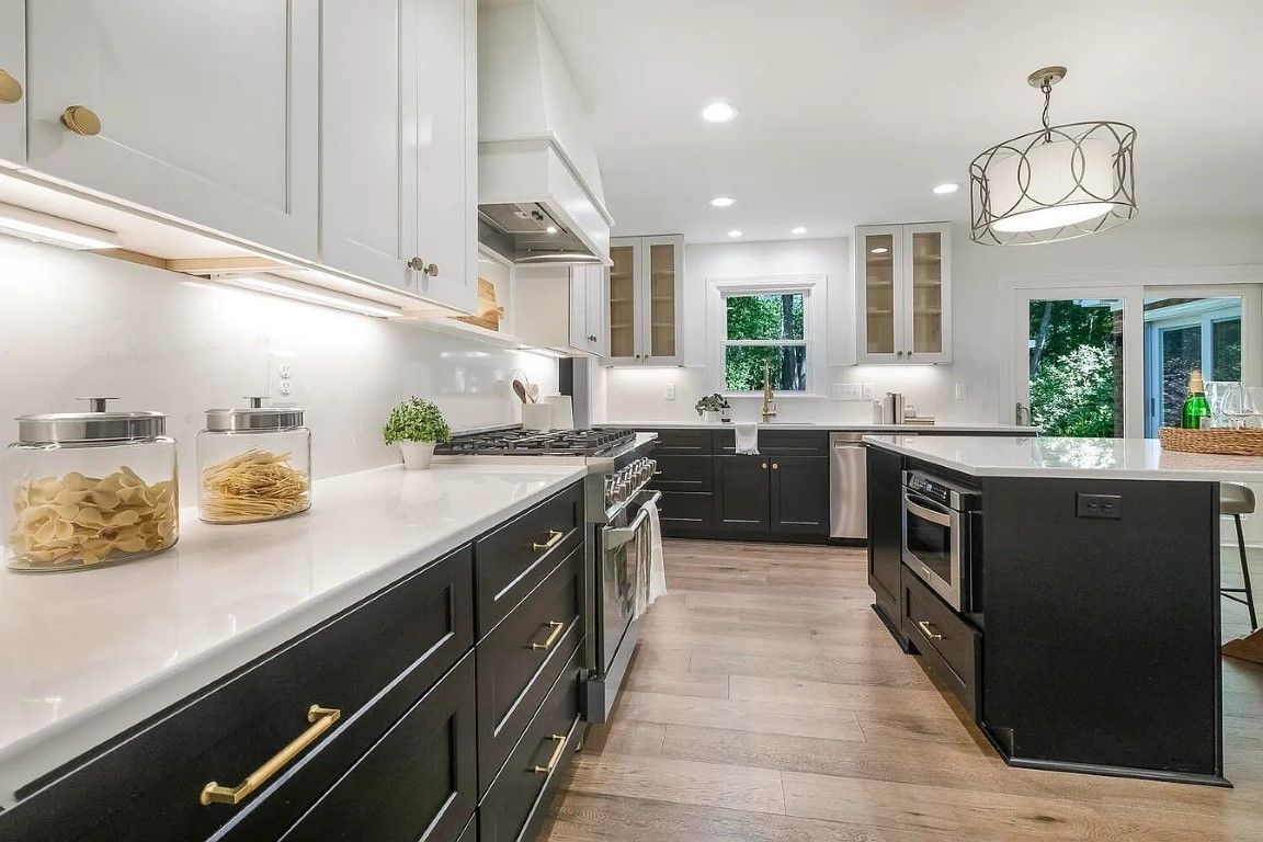 Modern kitchen with black and white cabinets, stainless steel appliances, and a central island.