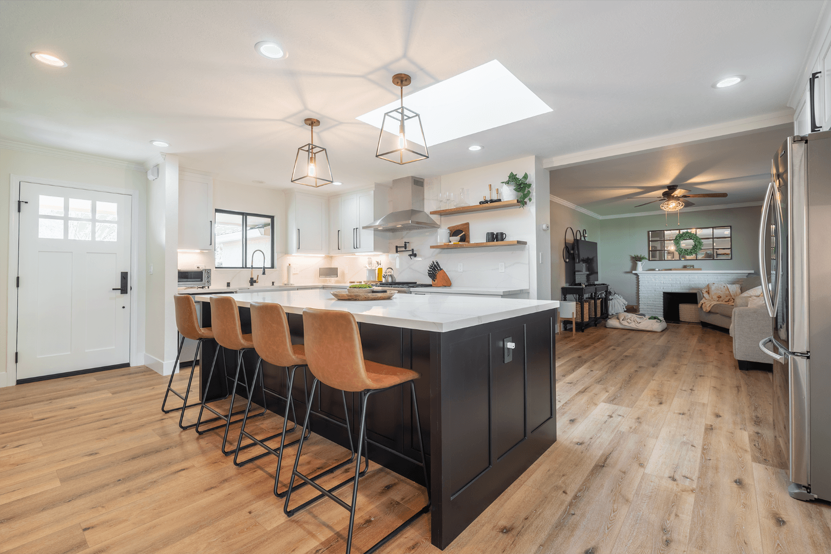 Spacious kitchen with a black island, brown bar stools, and white cabinets. Open to living room with hardwood floors.