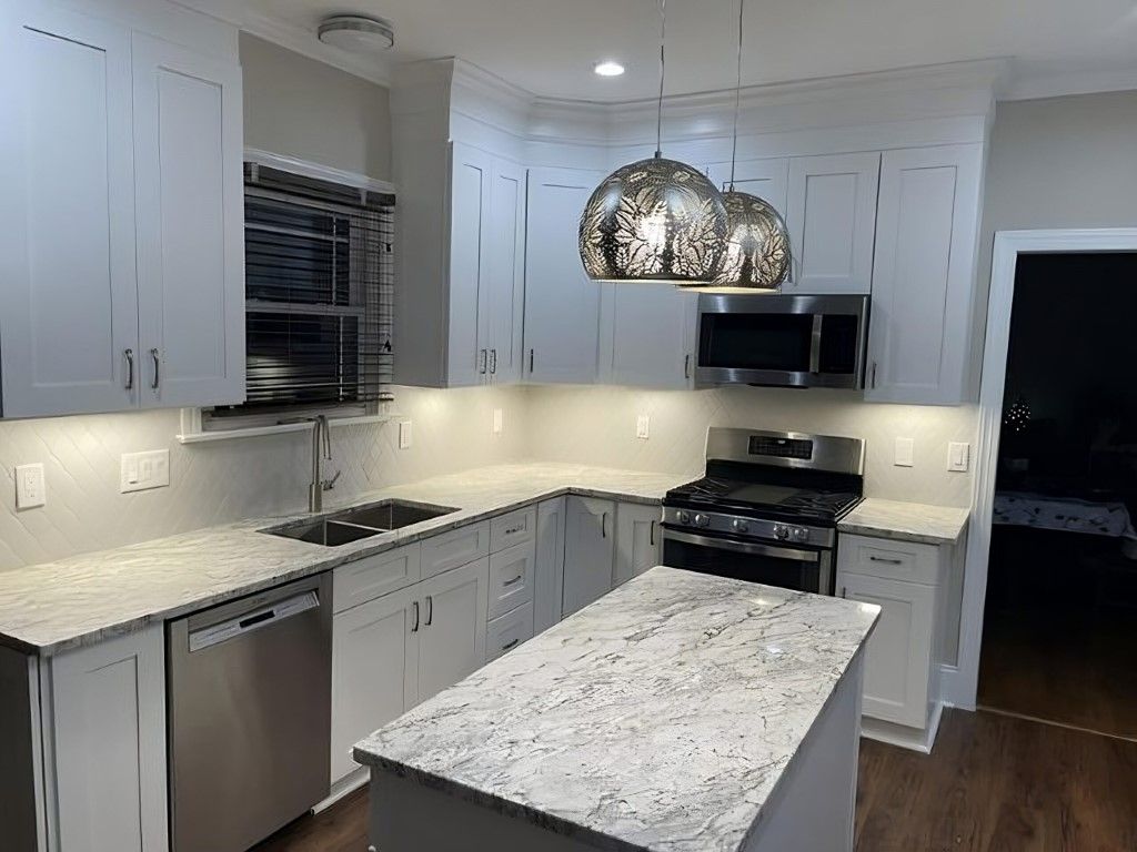 Modern white kitchen with stainless steel appliances, granite countertops, and pendant lights.