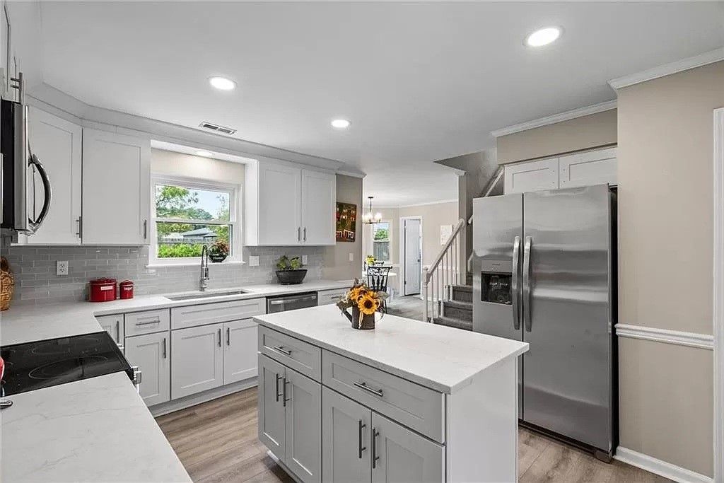 White kitchen with island, stainless steel refrigerator, and window overlooking greenery.