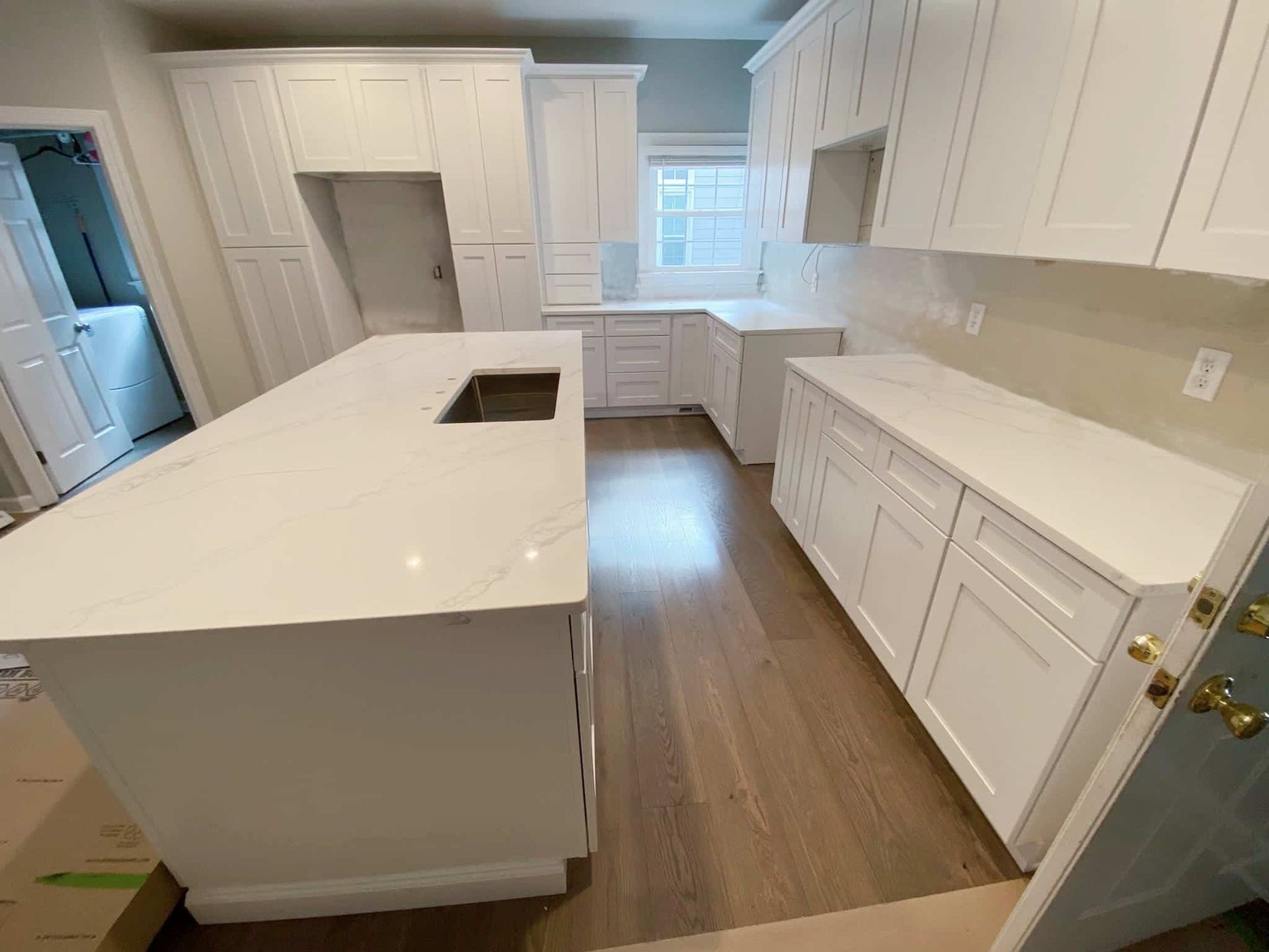 White kitchen with island, cabinets, countertops, and wood flooring; under construction.