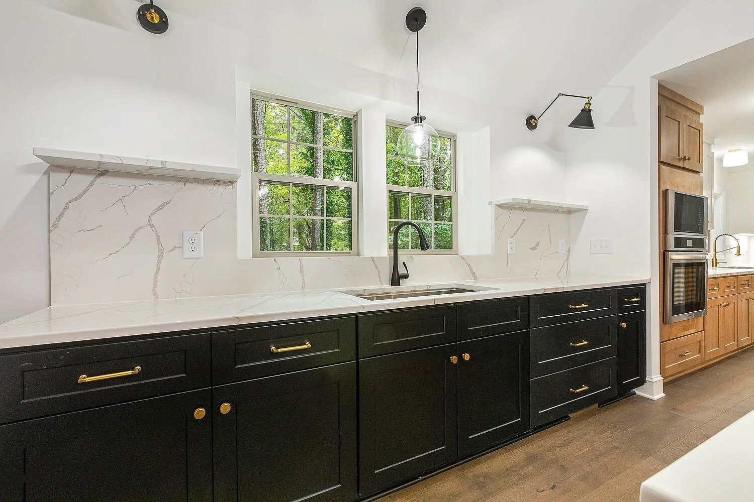 Modern kitchen with black cabinets, white countertops, and window overlooking trees.