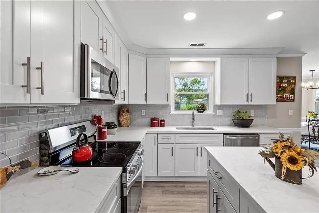 White kitchen with quartz countertops, cabinets, stainless steel appliances, and a window.