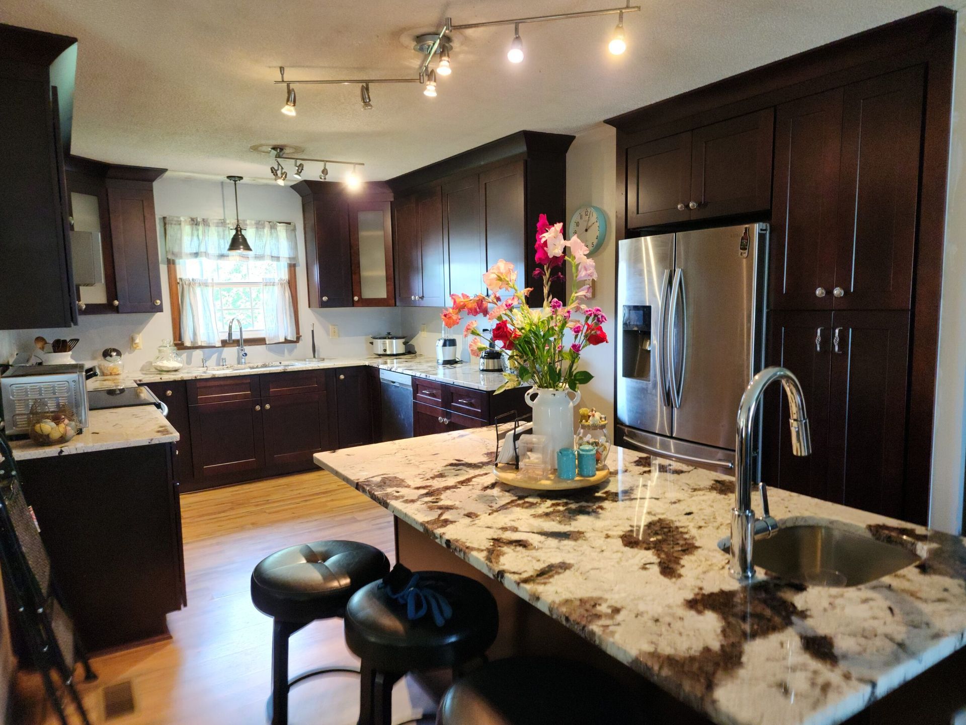 Kitchen with dark wood cabinets, granite countertops, and stainless steel appliances. Island with seating and flowers.