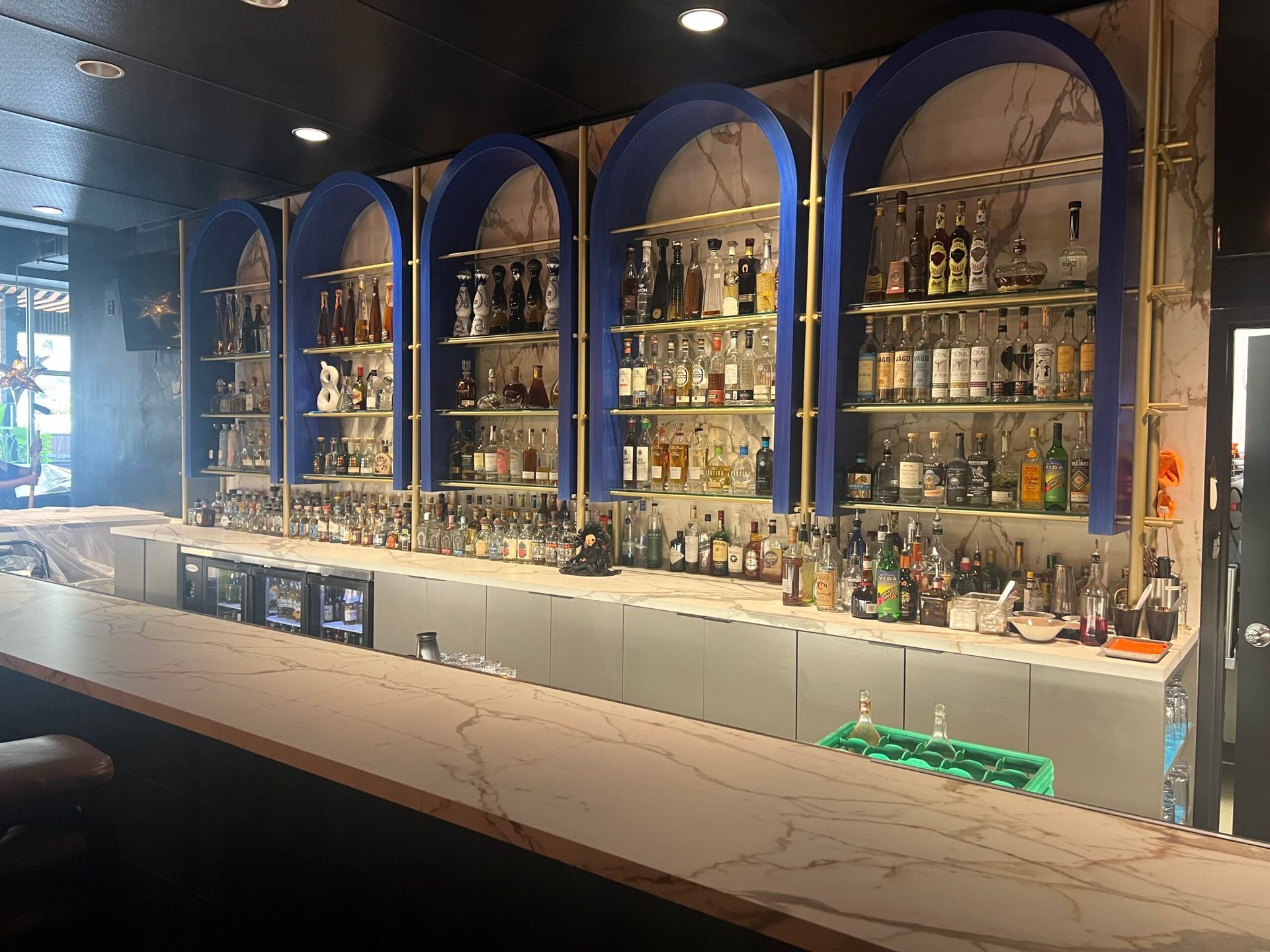 Bar interior with white countertops, marble and blue shelving, and bottles of alcohol.