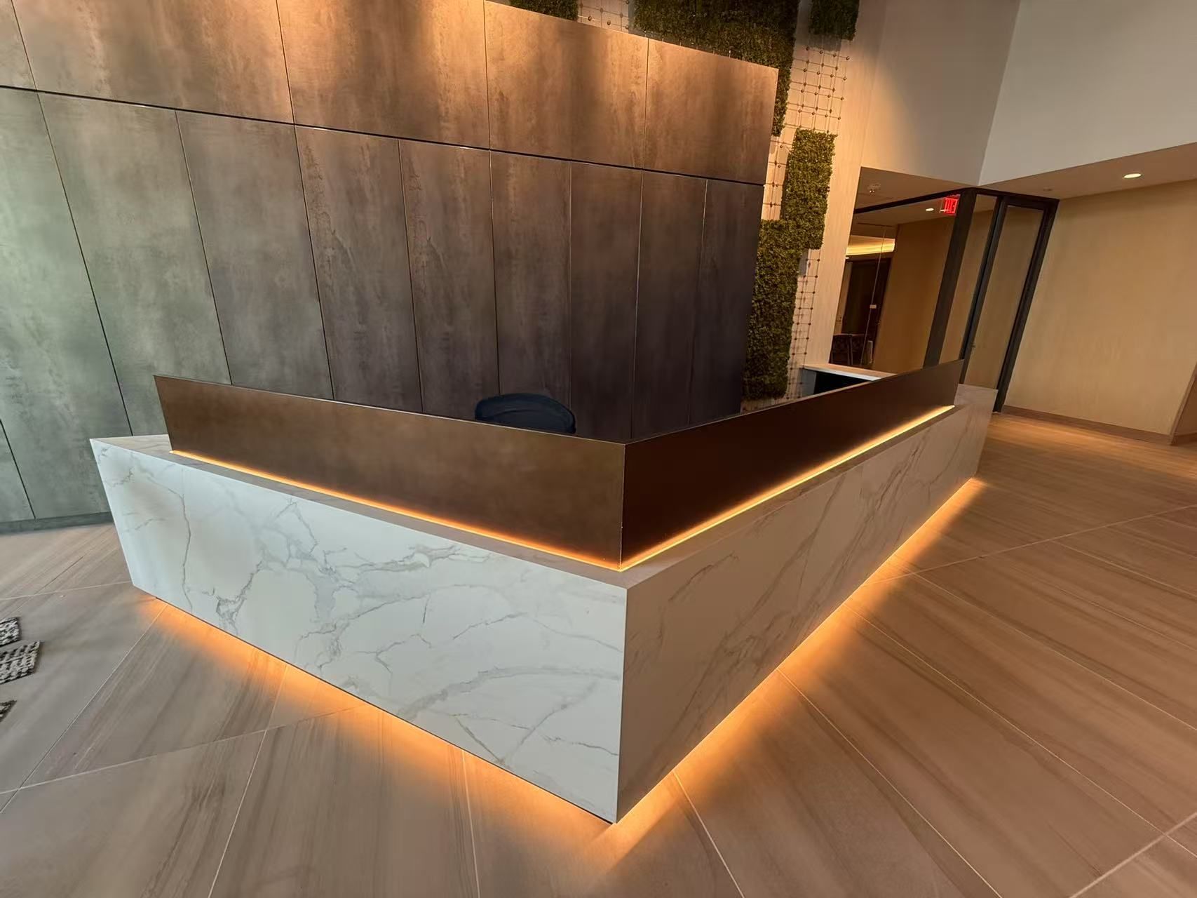 Modern reception desk with marble base, bronze top, and ambient lighting in a building lobby.