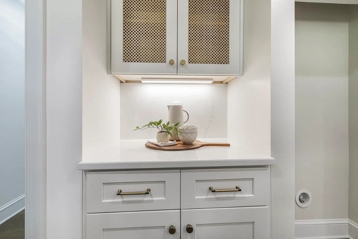 Built-in white cabinet with patterned doors, counter with decorations, and two lower cabinets.