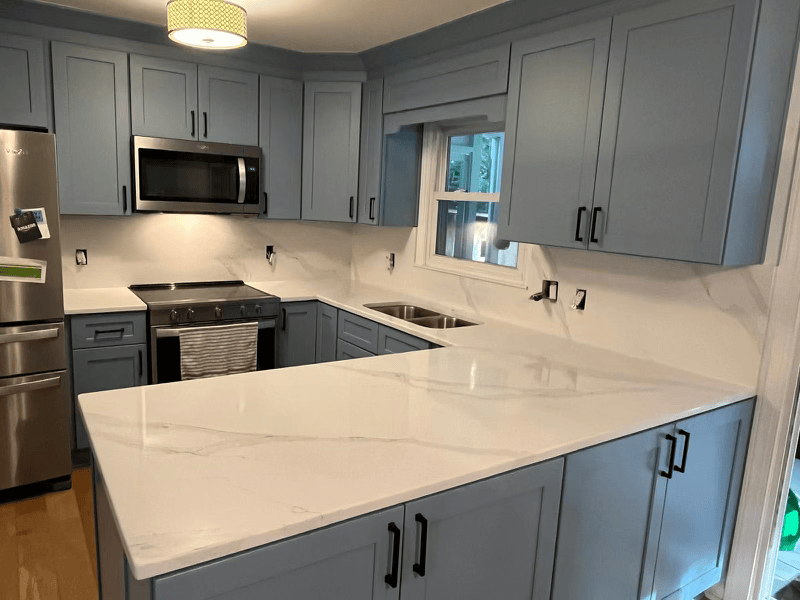 Blue kitchen with white countertops and stainless steel appliances.