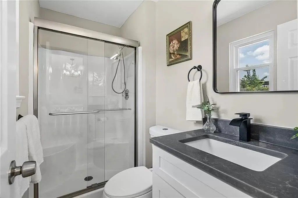 Bathroom with white cabinets, dark countertop, and glass shower.