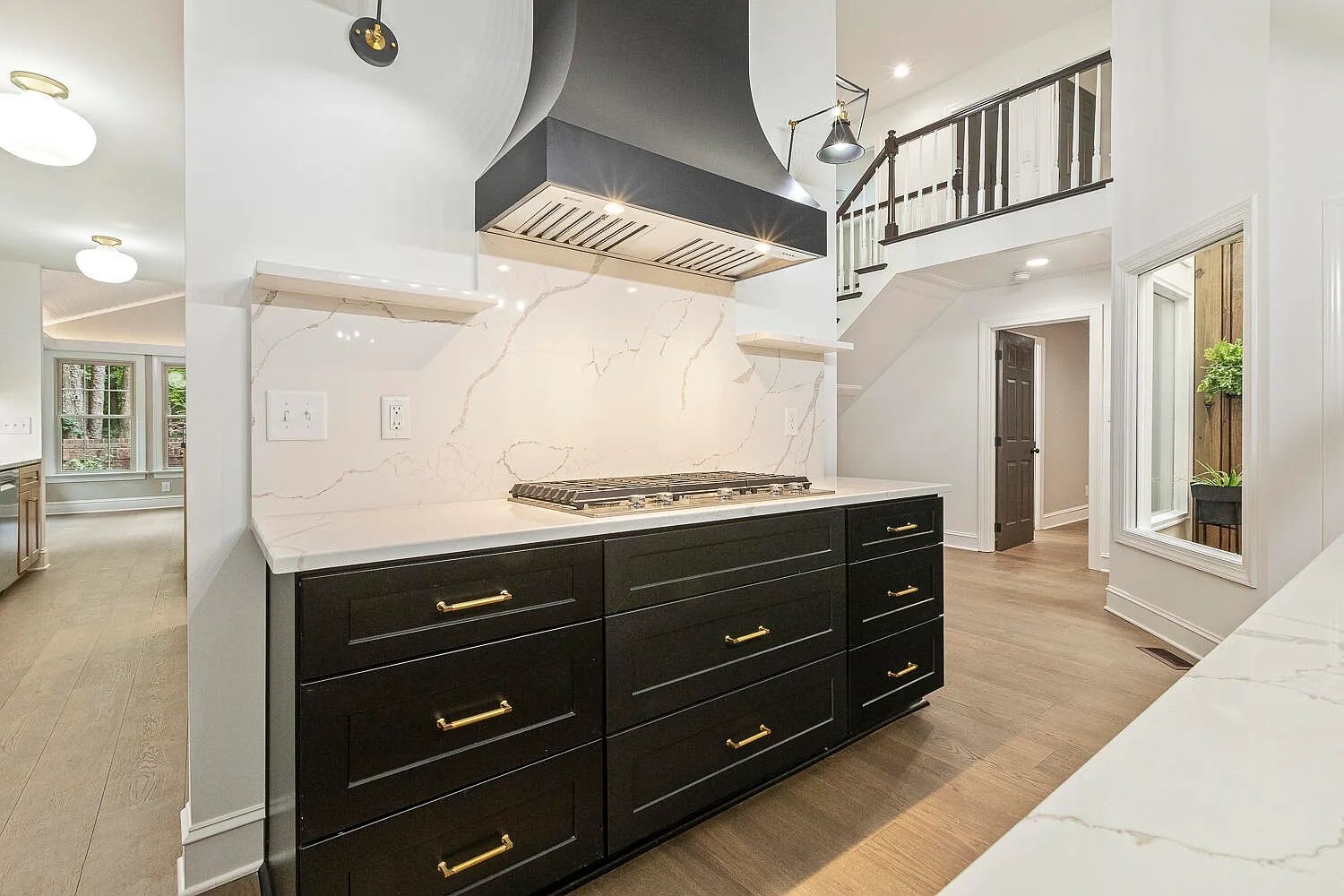 Modern kitchen with black cabinets, white countertop, range hood, and staircase.