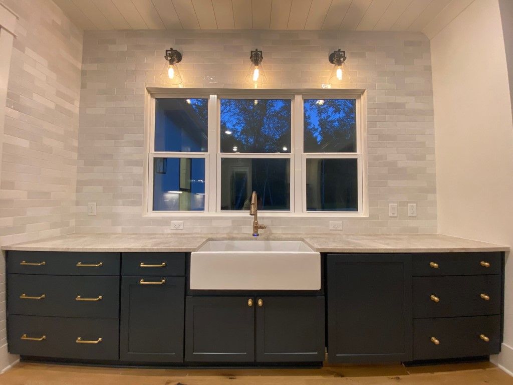 Kitchen with dark cabinets, a white farmhouse sink, and a window with three light fixtures above.