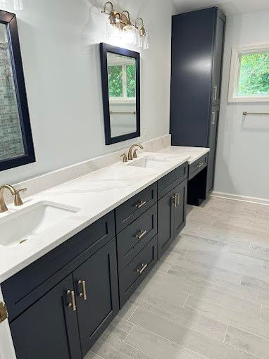 Bathroom with a dark navy vanity, white countertop, gold hardware, and a tall storage cabinet.