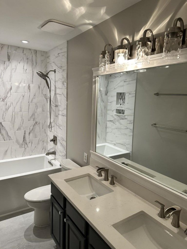 Bathroom with marble tile, gray walls, double sink vanity, tub, and toilet.