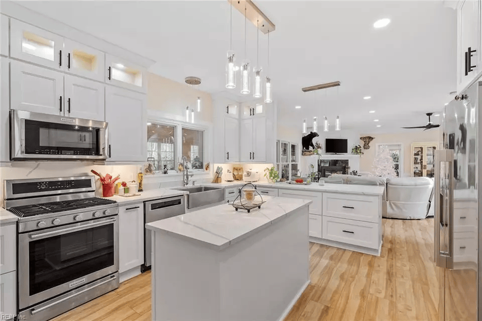 Bright white kitchen with stainless steel appliances, white cabinets, and island; wood floors.