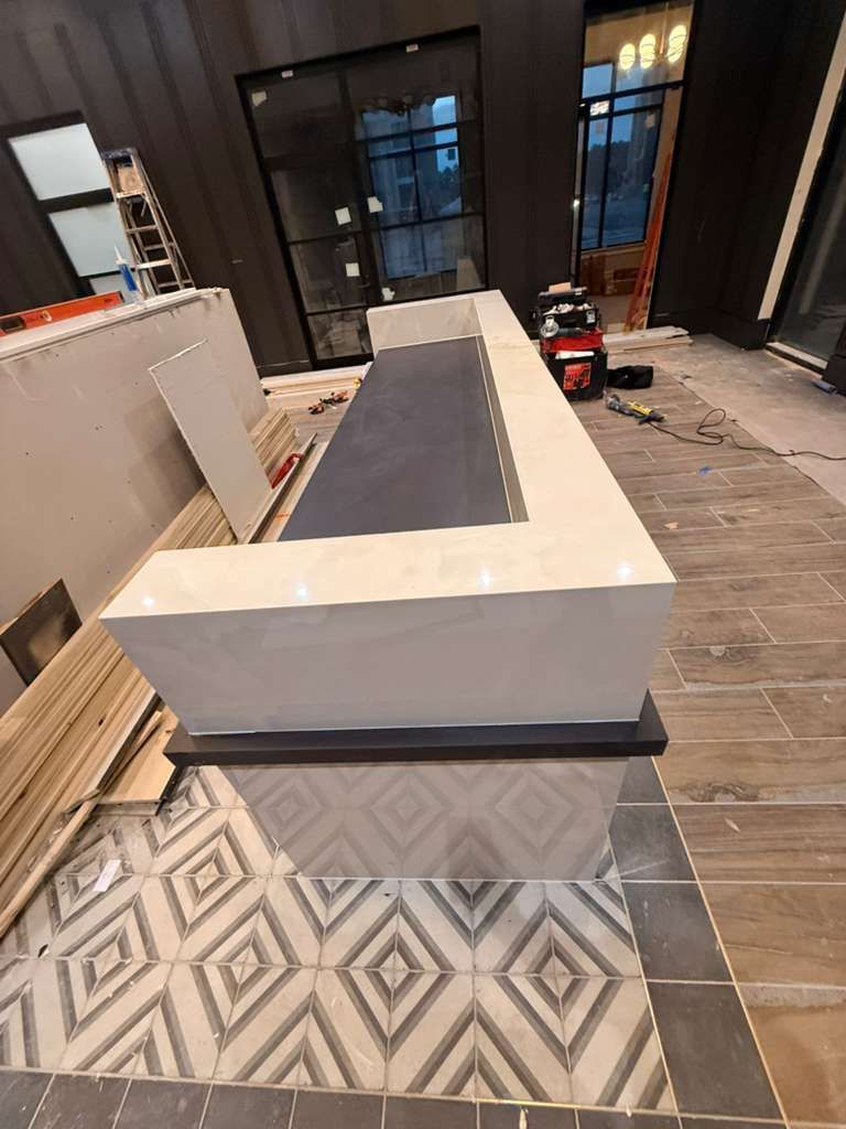 Bar with a white facade, black base, and gray countertop, on patterned tile floor, construction site.
