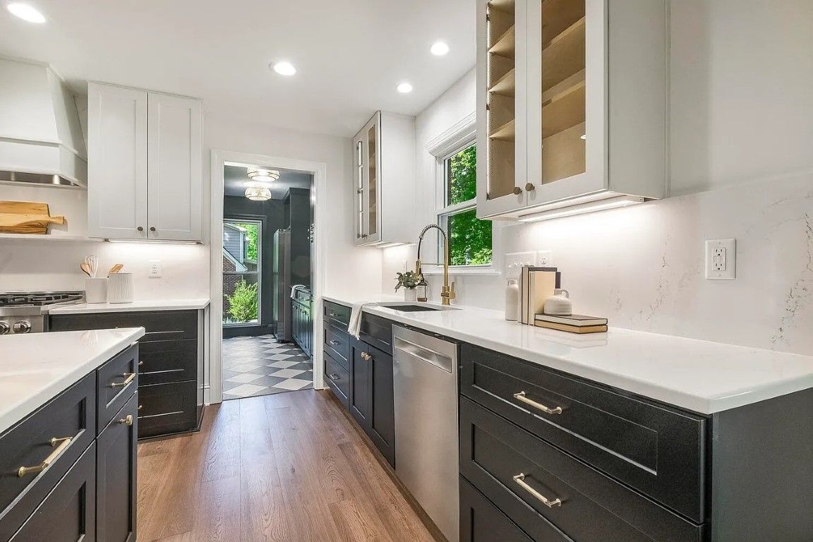 Modern kitchen with two-tone cabinets, stainless steel appliances, and a view through a doorway.