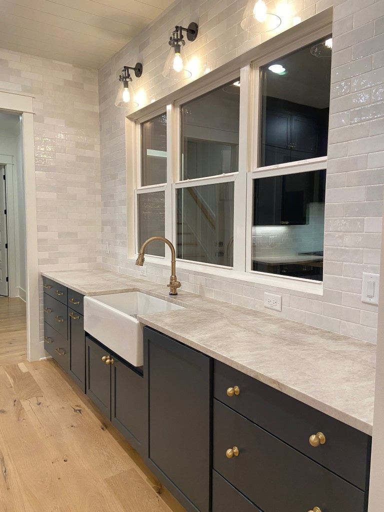 Kitchen with dark cabinets, white countertop, farmhouse sink, and white tiled wall.