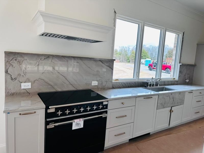 Kitchen with a black stovetop, white cabinets, marble backsplash, and a large window.